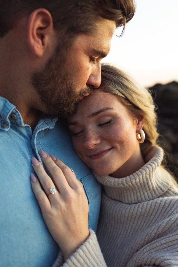 A man kisses the top of her head, her ring hand on his chest