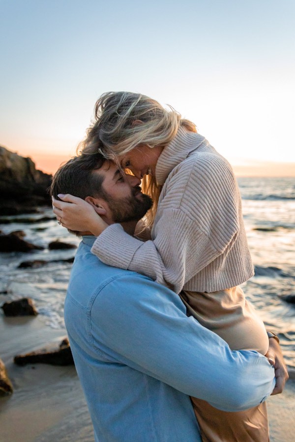 A couple hold each other at sunset on the rocks above the Pacific