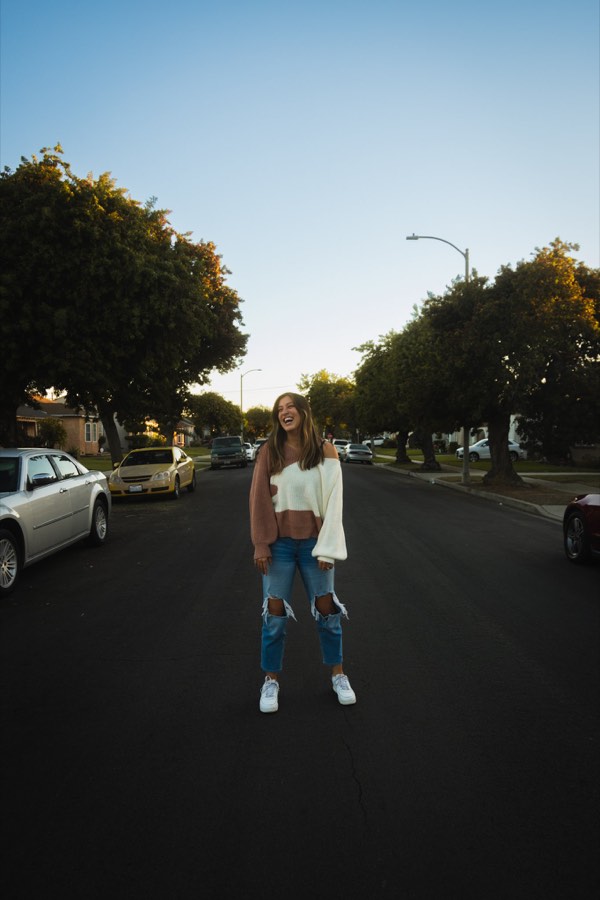 A woman standing alone in the middle of a tree-lined street