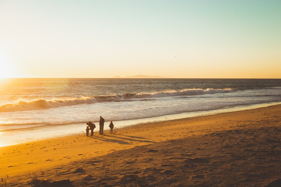 A golden beach at sunset with figures far down the shoreline