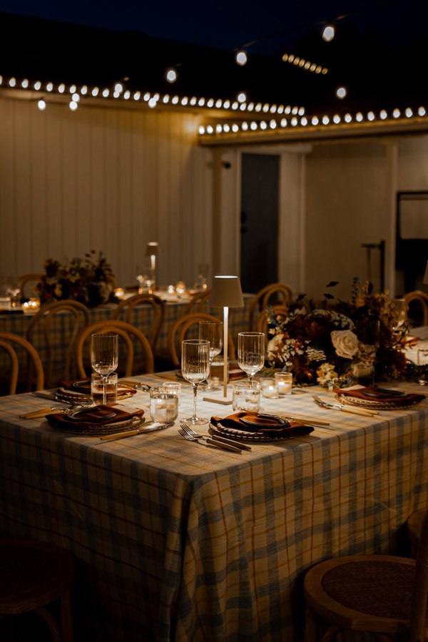 Reception tables laid for dinner under strings of warm light