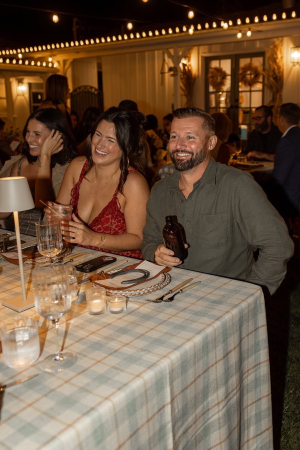 Guests laughing along a long reception table under string lights