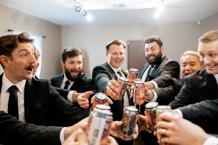 Groomsmen laugh as they reach in to toast with cans