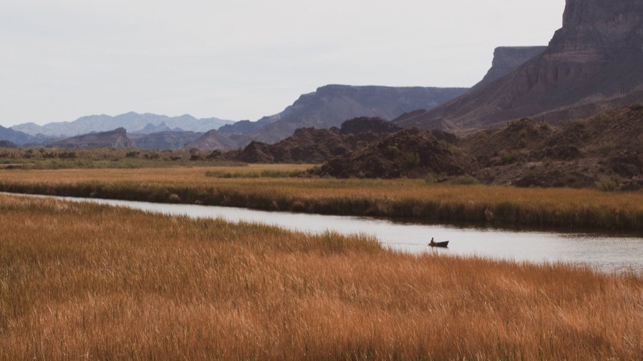 A wide marsh and river running below red rock mesas