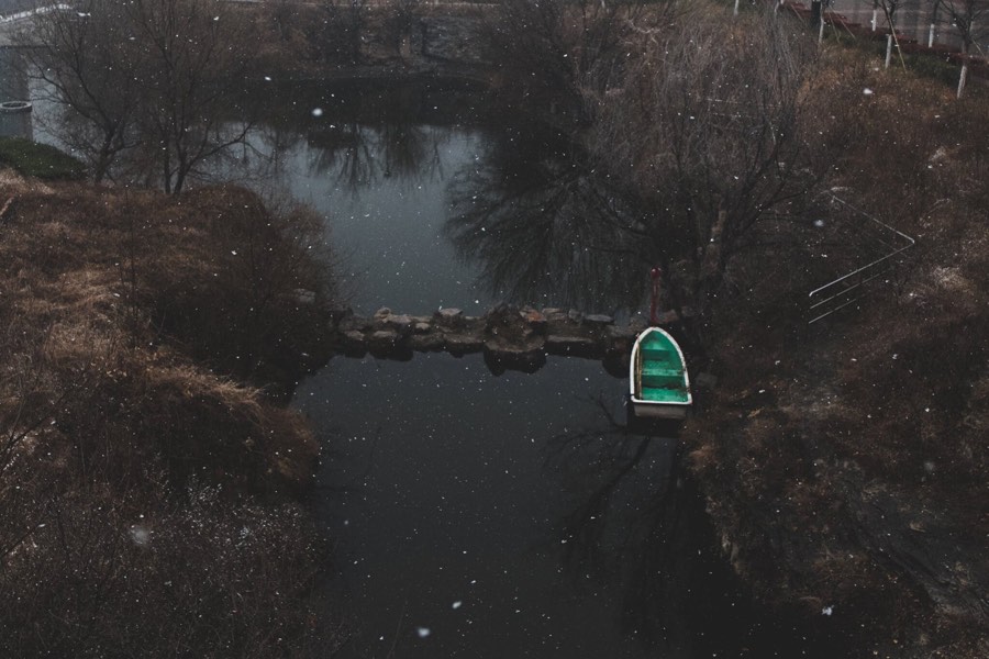 Aerial view of a small green boat on a dark winter pond