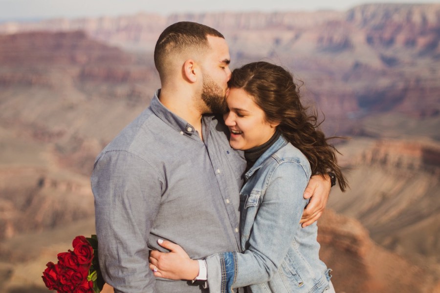 A couple hold each other at the Grand Canyon, roses still in hand