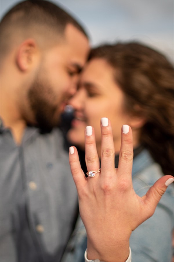 Two faces close together, an engagement ring on her hand