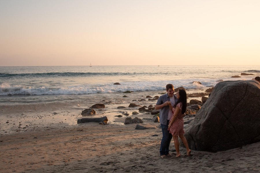 A couple hold each other beside a boulder on the evening beach