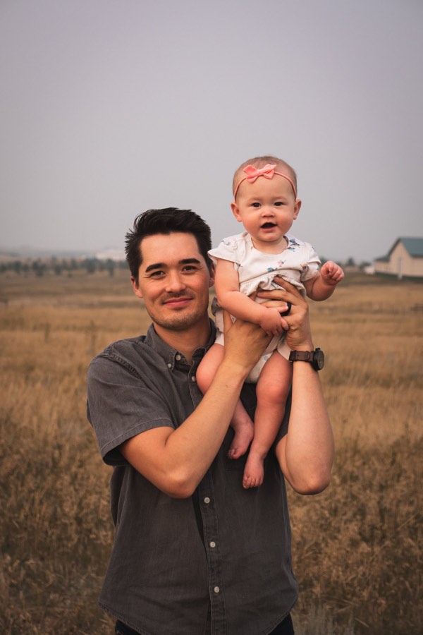 A man holds his baby up in a field of dry golden grass