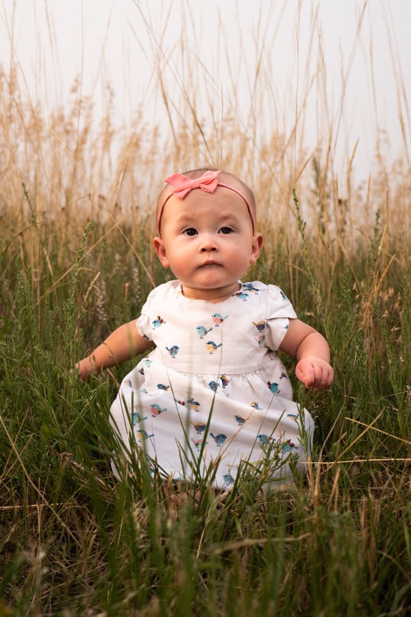 A baby sitting up in tall grass, looking straight to camera
