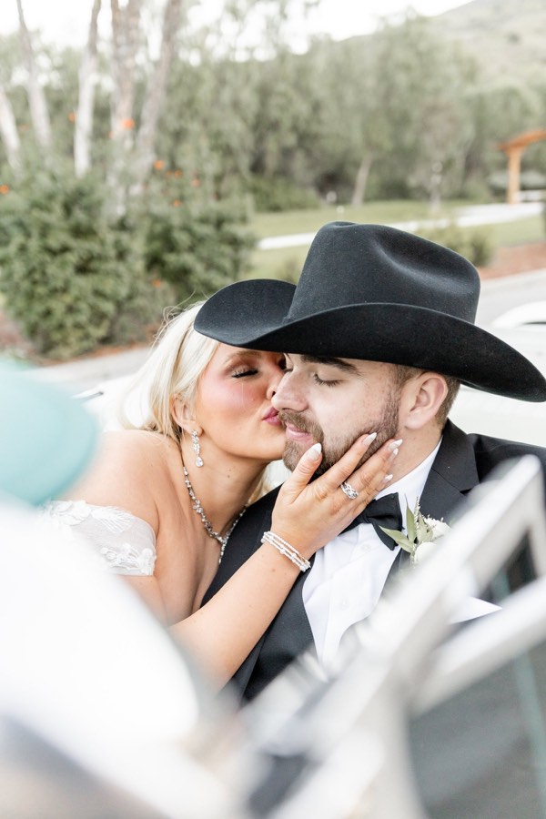 A bride and groom kiss, seen through the window of their car